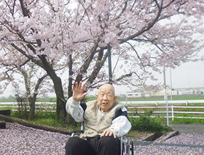 桜の木の下で手を振る高齢者。春の季節行事や屋外レクリエーション。